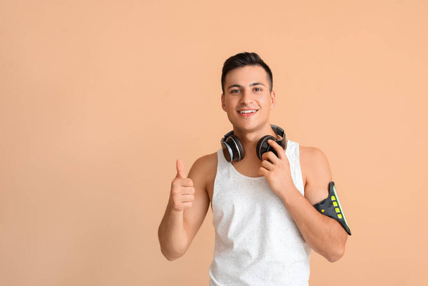 Sportieve jongeman met koptelefoon met duim-up op kleur achtergrond - Foto, afbeelding
