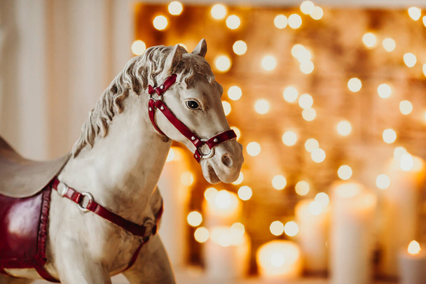 toy wooden rocking horse against the background of blurred lights in the fireplace - Photo, Image