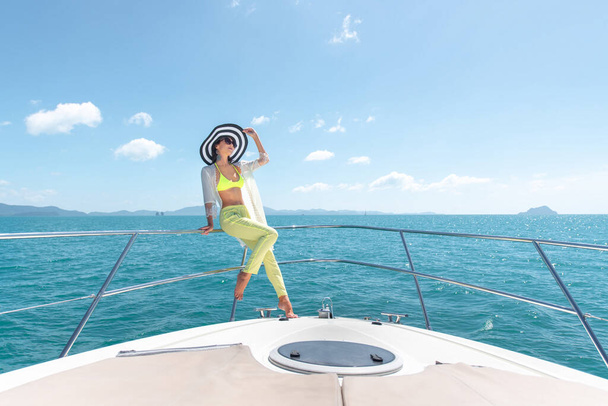 Outdoor shot of adorable young woman in a summer suit and hat sitting on edge of yacht, looking to beautiful nature landscape during trip. Happy woman enjoying summer travel. Back view - Fotoğraf, Görsel
