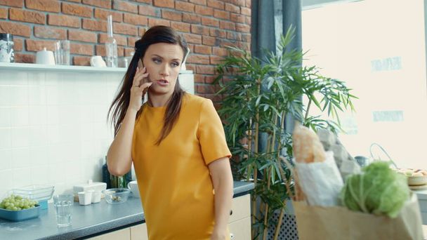 Ideges nő kipakol a bevásárlótáskából a konyhában. Nő beszél telefon érzelmileg. - Fotó, kép
