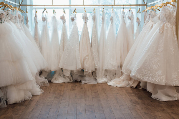 beautiful white wedding dresses on hangers in the store - Fotoğraf, Görsel