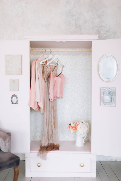 女性の服、オープンドア、装飾、ミラー、バッグ、ハンガー、明るい部屋、コンセプト、花繊細なパステルカラーのシルクドレスのための木製ピンクのワードローブ - 写真・画像