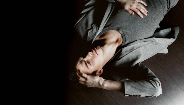 Retrato de um belo modelo masculino de cabelos escuros em uma jaqueta cinza e t-shirt encontra-se no chão - Foto, Imagem