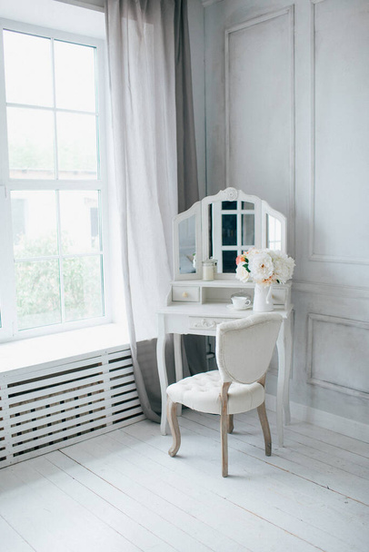 όμορφο λευκό εσωτερικό. κλασικό δωμάτιο με ξύλινο πάτωμα φως τοίχους με καλούπια, τουαλέτα με καθρέφτη, διακοσμημένο με διακόσμηση και λουλούδι - Φωτογραφία, εικόνα