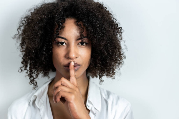 hermosa mujer afroamericana haciendo gesto de silencio con el dedo en los labios con fondo blanco - Foto, Imagen