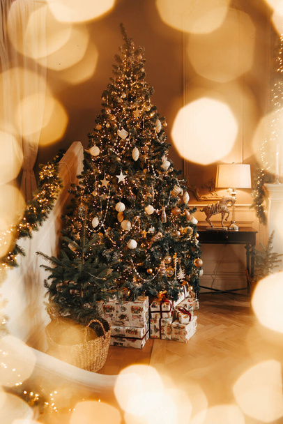 Luxe cosy et chaleureux décoration intérieure de la salle de Noël, arbre de Noël décoré par des lumières présente des jouets cadeaux, des bougies, des lanternes, cheminée à éclairage guirlande, salon de vacances. - Photo, image