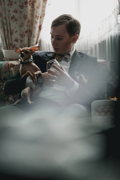handsome man in black jacket sitting and hugging small dog - Φωτογραφία, εικόνα