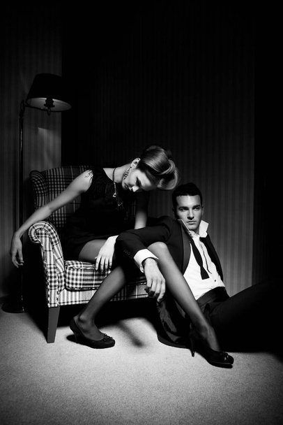 Beau couple passionné en tenue classique dans l'ombre dans la pièce : femme sur chaise, homme sur le sol à ses pieds - Photo, image