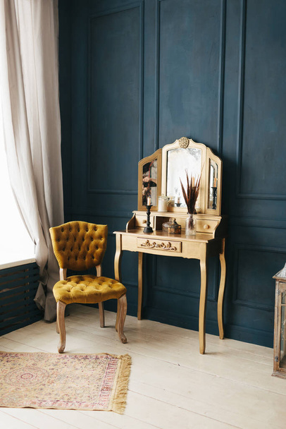 hermoso vintage colorido interior. habitación clásica con suelo de madera paredes azules con molduras, tocador de oro con espejo decorado con elementos y silla amarilla - Foto, Imagen