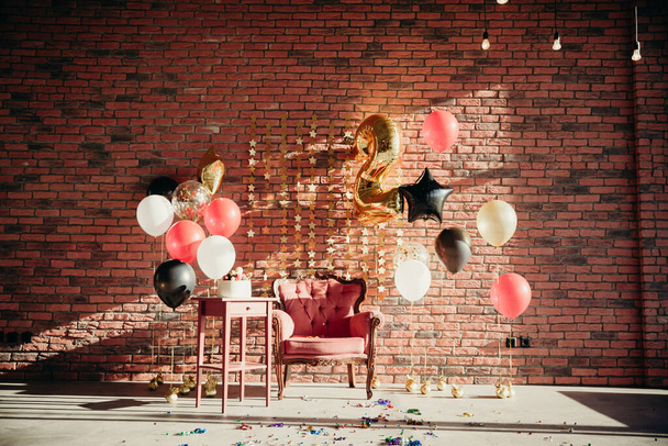 in honor of the child birthday 2 years, studio in the loft style, filled with sunlight. classic orange chair, table with cake, red, black, gold balloons against a brick wall background - Fotoğraf, Görsel