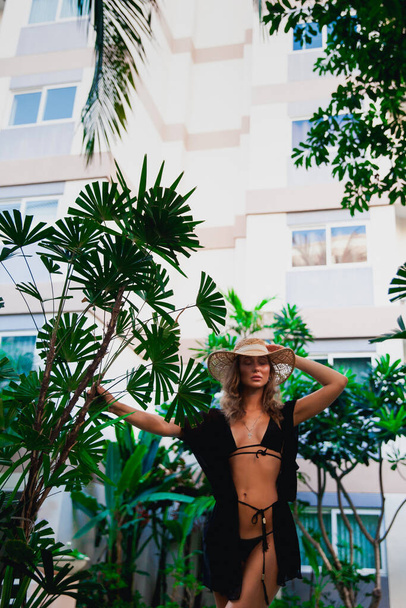 stylish beautiful woman in bikini posing near plants and swimming pool - Photo, Image