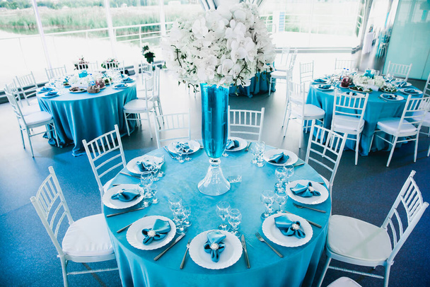 piękna restauracja na weselu w niebiesko-białych kolorach, obrusy serwowane z obrusem, serwetki tekstylne kwiaty storczyki w wazonach z niebieską wodą - Zdjęcie, obraz