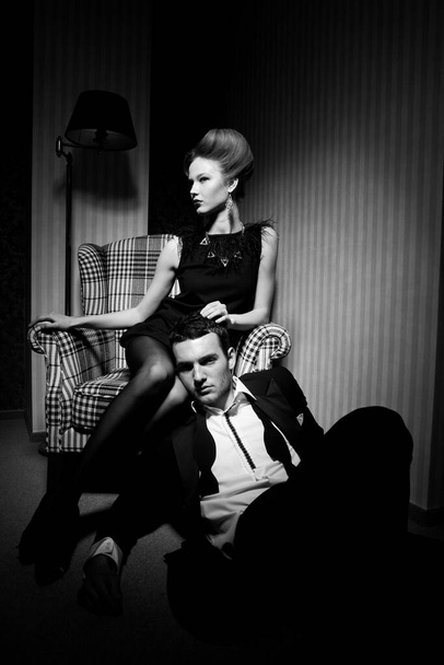 Красива пристрасна пара в класичному одязі в тіні в кімнаті: жінка на стільці, чоловік на підлозі біля її ніг
 - Фото, зображення