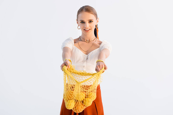 elegant blonde woman giving string bag with citrus fruits isolated on white - Fotoğraf, Görsel