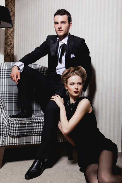 Beau couple passionné en tenue classique dans l'ombre dans la pièce : homme sur la chaise, femme sur le sol à ses pieds - Photo, image