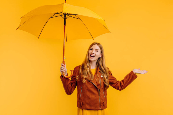 Happy cheerful girl in a yellow dress and autumn jacket, laughing and rejoicing with a yellow umbrella on a yellow background. Autumn concept - Photo, image