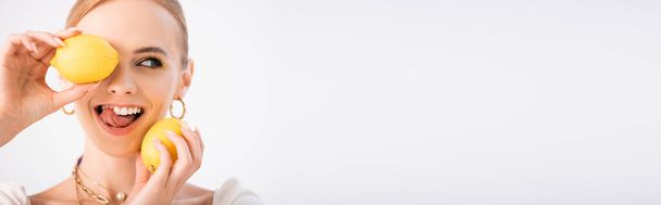 mulher loira engraçada segurando limões e mostrando língua isolada em branco, tiro panorâmico - Foto, Imagem