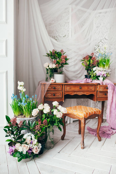 vintage décoré avec des fleurs de printemps en tissu violet et des verts sur des meubles anciens en bois avec tiroirs dans une chambre classique sur un plancher en bois blanc près de grandes fenêtres et rideaux en tulle - Photo, image