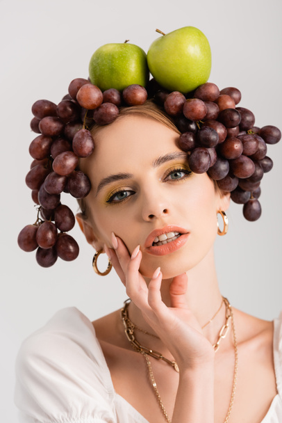 portrait of rustic blonde woman posing with grapes and apples on head isolated on white - Foto, afbeelding