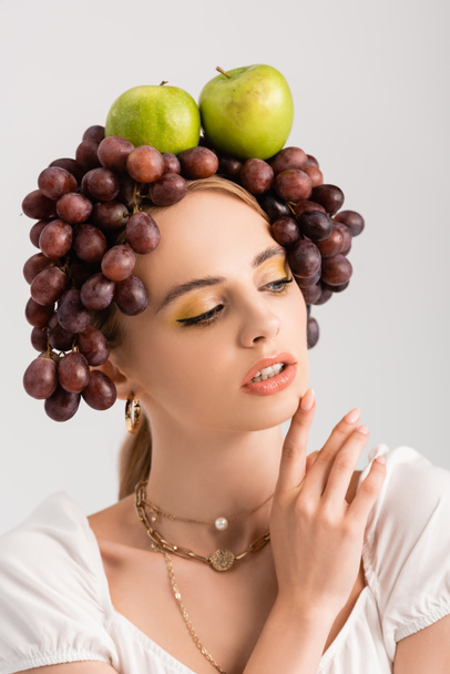 portrait of rustic blonde woman posing with grapes and apples on head isolated on white - Zdjęcie, obraz