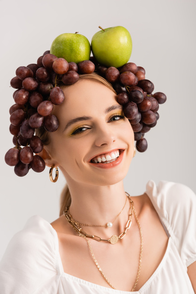 portrait of rustic blonde woman posing with grapes and apples on head isolated on white - Foto, Imagen