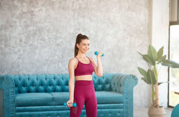 Chica en forma feliz en ropa deportiva haciendo ejercicios con mancuernas en casa - Foto, Imagen
