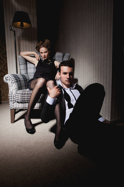 Belo casal apaixonado em roupas clássicas nas sombras da sala: mulher na cadeira, um homem no chão a seus pés - Foto, Imagem