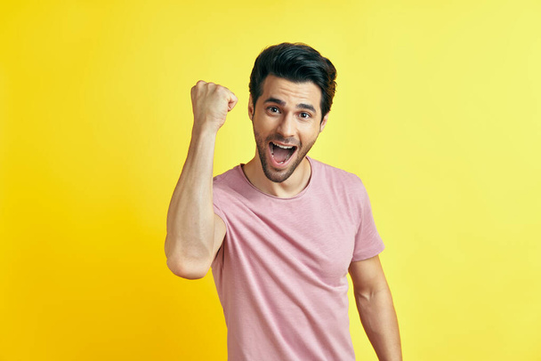 Happy man celebrating his success with winner gesture on yellow background - Photo, image