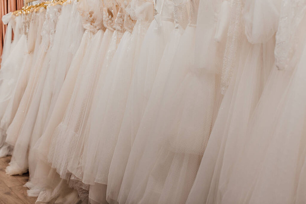 beautiful white wedding dresses on hangers in the store - Fotó, kép