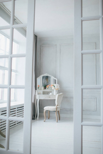 belo interior branco. quarto clássico com piso de madeira paredes leves com molduras, penteadeira com espelho, decorado com decoração e flor - Foto, Imagem