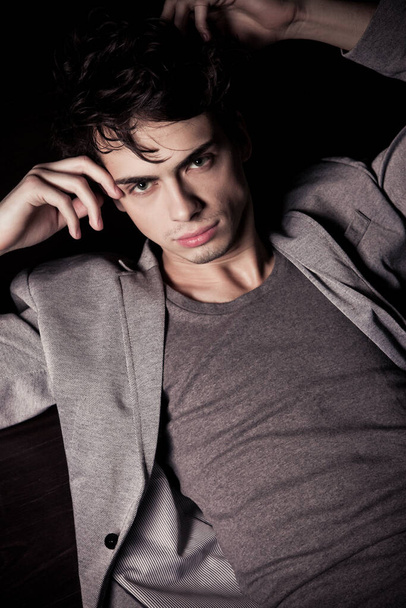 Portrait of a handsome male model of a dark-haired in a gray jacket and t-shirt lies on the floor - Foto, Imagen