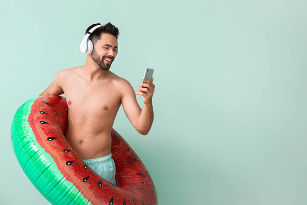 Νεαρός άνδρας με ακουστικά, φουσκωτό δαχτυλίδι και κινητό τηλέφωνο στο φόντο χρώμα - Φωτογραφία, εικόνα