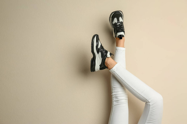 Woman wearing sneakers on beige background, closeup. Space for text - Φωτογραφία, εικόνα