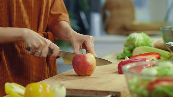 A nő keze vörös almát vág a konyhában. Háziasszony főzés növényi saláta. - Fotó, kép