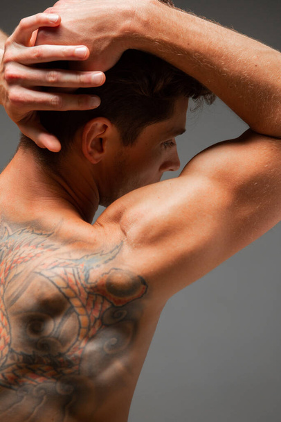 Portrait of handsome young guy with stylish haircut without shirt standing in studio. Body with tattoo. View from back - Zdjęcie, obraz