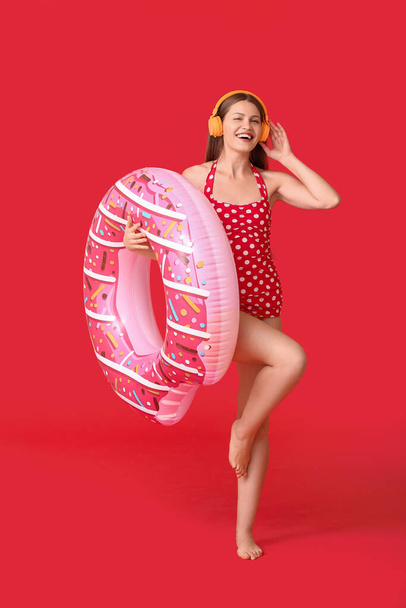 Mujer joven con auriculares y anillo inflable sobre fondo de color - Foto, imagen