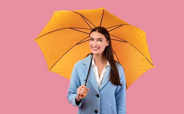 Portrait of cute girl holding umbrella at pink studio - Foto, immagini