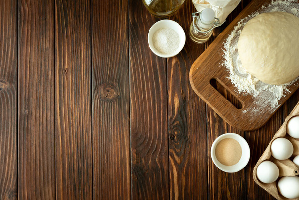 Baking in rural kitchen. Dough and recipe ingredients on vintage brown wooden table. Top view. Rustic background - Foto, Bild