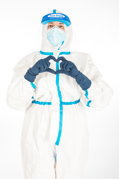 Ženská doktorka nosící OOP, aby bojovala s koronavirem, dělá srdce rukou, na bílém pozadí. Válečníku. Koncept medicíny COVID - Fotografie, Obrázek