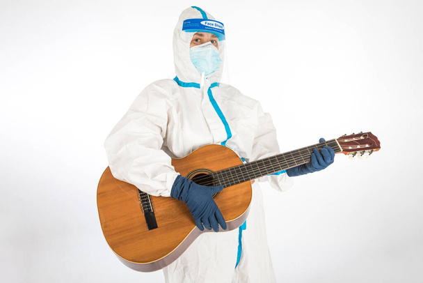 Doctor woman wearing PPE to fight coronavirus, playing guitar, on white background. Warrior. COVID medicine concept - Photo, Image