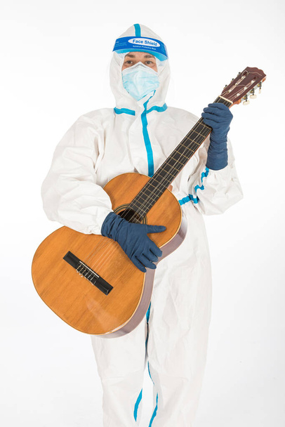 Doctor woman wearing PPE to fight coronavirus, playing guitar, on white background. Warrior. COVID medicine concept - Photo, Image
