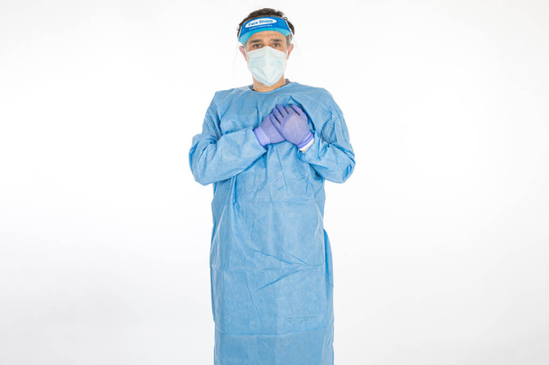 Doctor wearing blue PPE to fight coronavirus, with his hands on his heart, on white background. Warrior. COVID medicine concept - Photo, Image