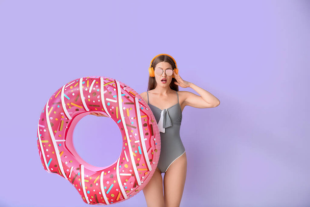 Überraschte Frau mit Kopfhörer und aufblasbarem Ring auf farbigem Hintergrund - Foto, Bild