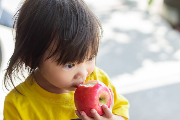 Portrait Bild von 2 Jahre alt von Baby. Glückliches asiatisches Mädchen, das einen roten Apfel isst und beißt. Genießen Sie den Moment. Gesundes Essen und Kinderkonzept. Vintage-Stil. - Foto, Bild
