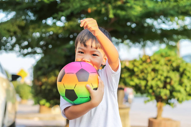 Imagem de retrato de 5 menino. Menino asiático feliz brincando e segurando um brinquedo de futebol em suas mãos. Ele usa camisa branca no parque infantil. Rapaz feliz e sorridente. Esporte e conceito de criança. - Foto, Imagem