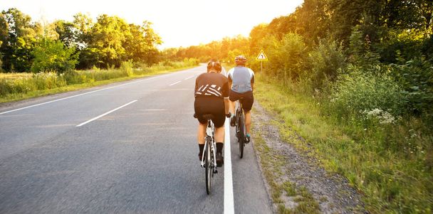 Two cyclist riding through the asphalt road in sunset - Foto, afbeelding