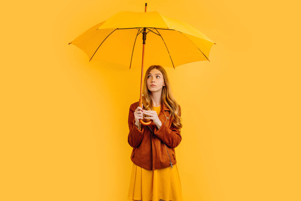 Beautiful girl with a yellow umbrella, with a thoughtful face - Фото, изображение