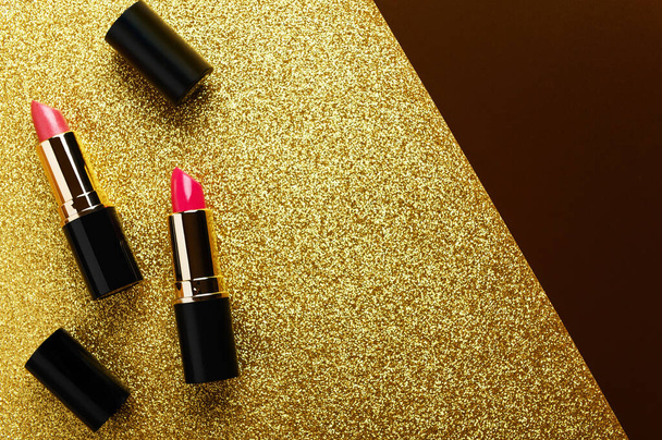 Lipsticks bovenaanzicht op gouden glanzende achtergrond. Modieuze rode lipgloss op glinsterende sequin platte lay achtergrond. Creatieve luxe cosmetica, make-up accessoire advertentie met tekstruimte. - Foto, afbeelding