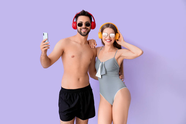 Młoda para ze słuchawkami i telefonem komórkowym na kolorowym tle - Zdjęcie, obraz