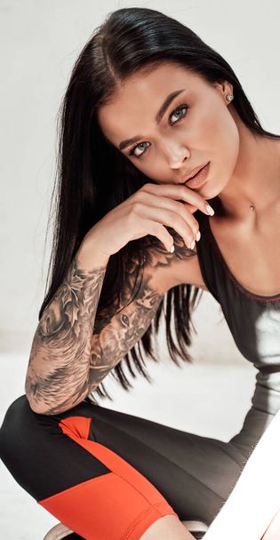 Roztomilá a krásná brunetka dívka s tetováním v černé teplákové soupravě - Fotografie, Obrázek